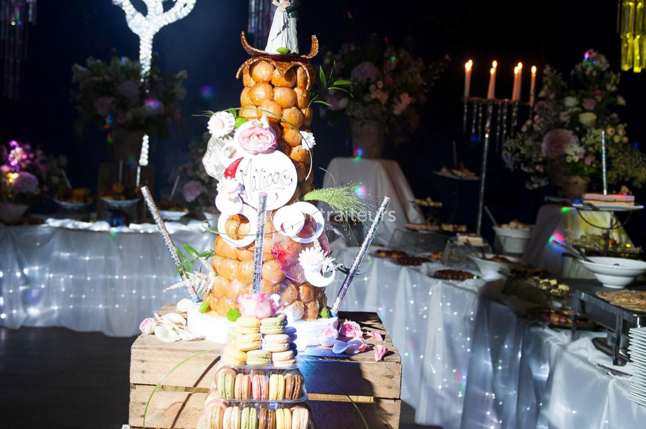 Pièce montée en choux décorée de fleurs et de macarons, entourée de bougies et de tables de réception.