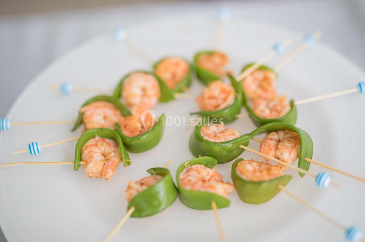 Crevettes grillées enroulées dans des morceaux de poivron vert, présentées sur des piques en bois sur une assiette blanche.