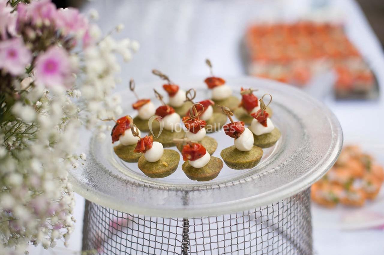 Plateau de bouchées apéritives surmontées de fromage et de tomates cerises, posé sur une table décorée de fleurs.
