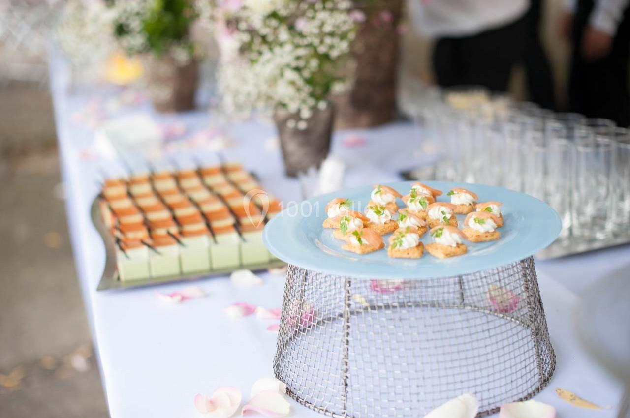 Plateau de canapés au saumon et fromage frais sur une table décorée de fleurs, avec d'autres amuse-bouches en arrière-plan.