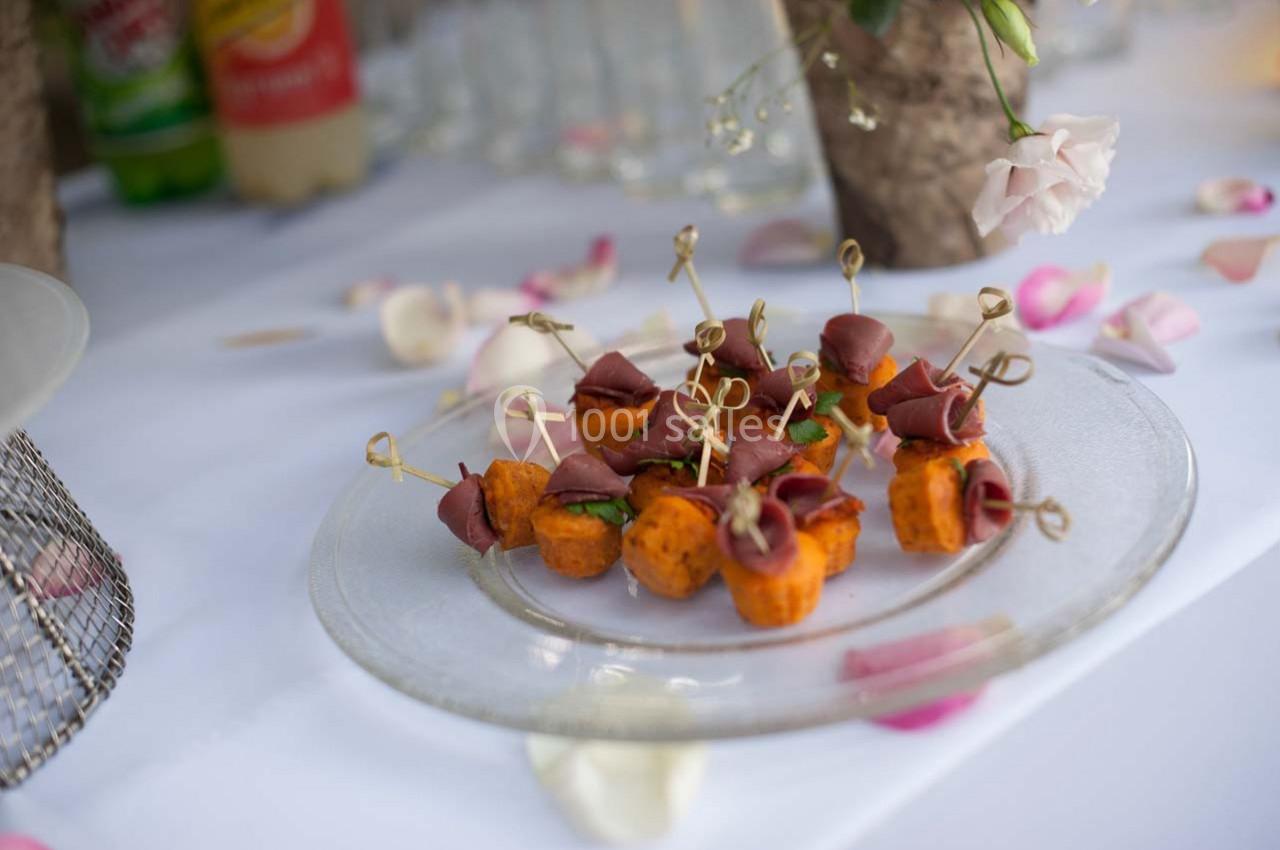 Assortiment de bouchées apéritives sur un plateau en verre, décoré de pétales de fleurs sur une nappe blanche.