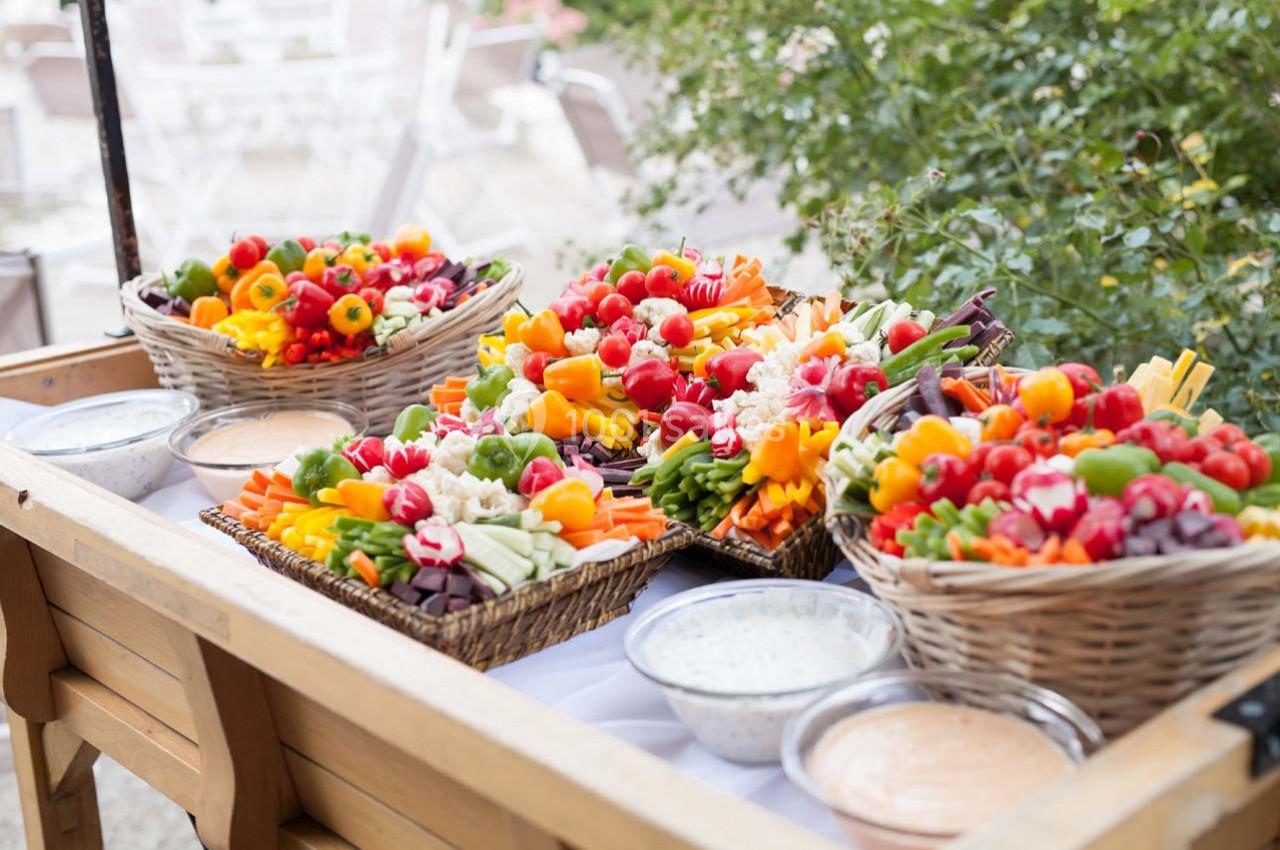 Plateaux de légumes colorés avec trempettes, disposés sur une table en extérieur près de végétation.
