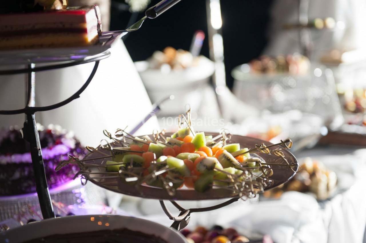 Plateau de fruits frais coupés en morceaux, présenté sur une table de buffet avec d'autres plats en arrière-plan.