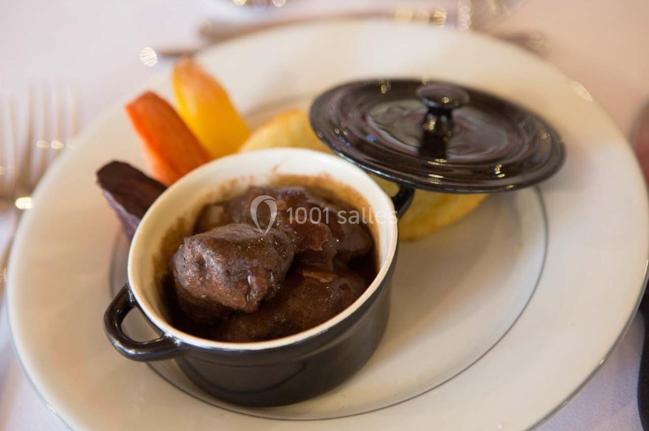 Plat de bœuf mijoté servi dans une cocotte noire, accompagné de légumes et d'une garniture sur une assiette blanche.