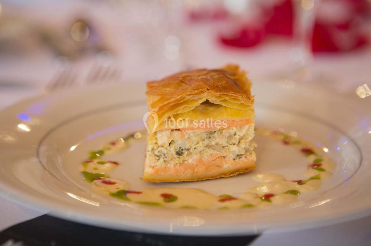 Part de feuilleté au saumon et farce crémeuse, servie sur une assiette avec une sauce décorative colorée.