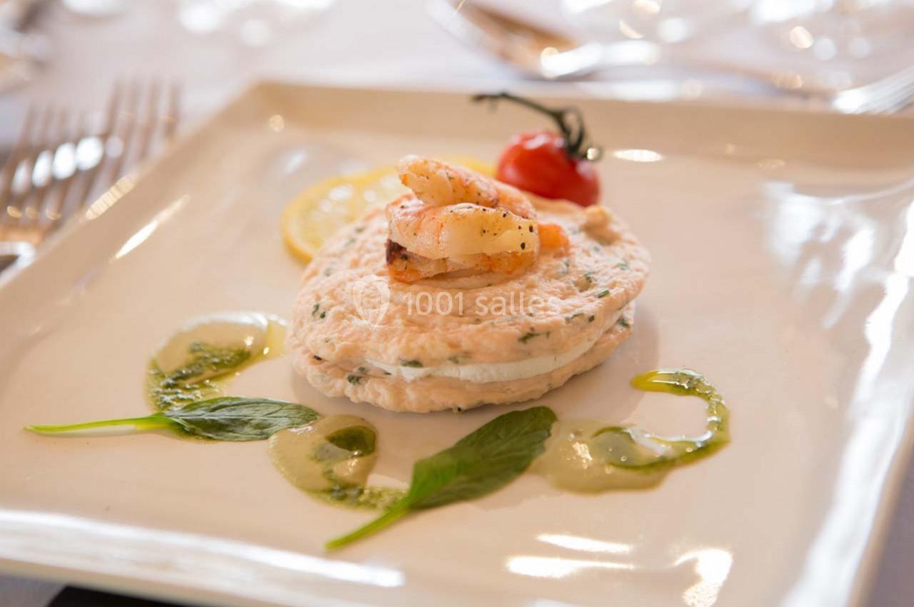 Plat gastronomique composé d'une mousse de poisson garnie de crevettes, tomate cerise et sauce verte décorative.