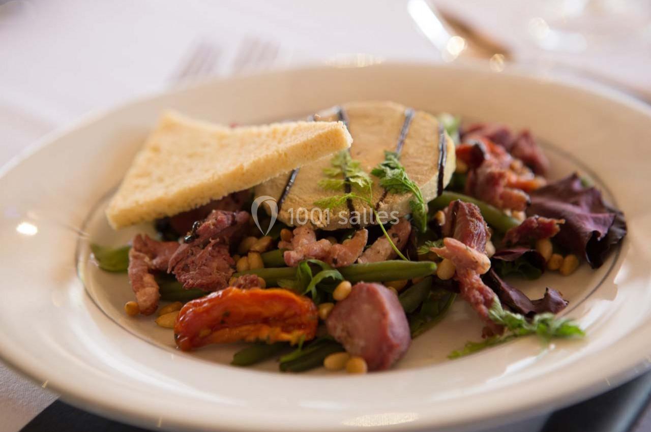 Assiette de salade composée avec légumes, viande, croûtons et fromage, présentée sur une table dressée.