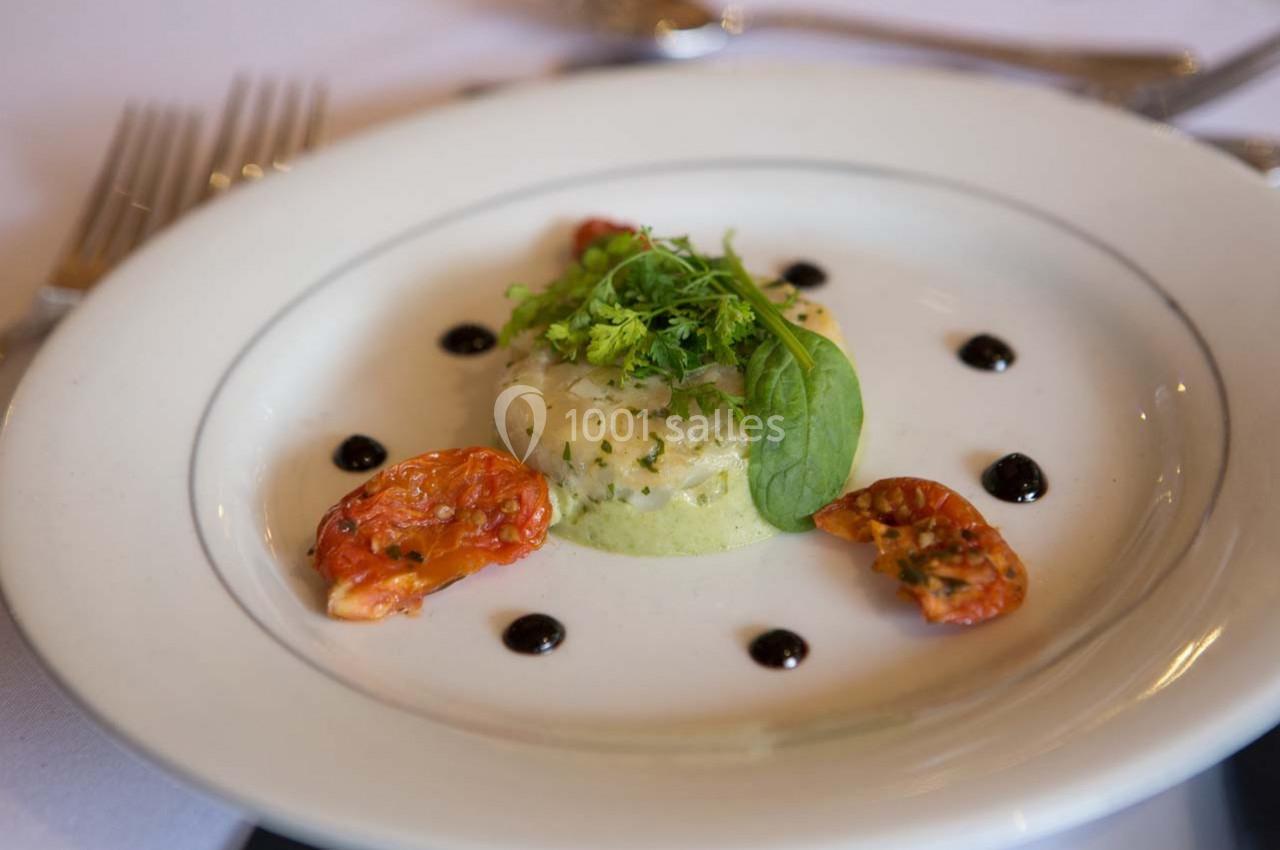 Plat gastronomique composé d'une mousse verte, de tomates confites, de sauce en points et de verdure en décoration.