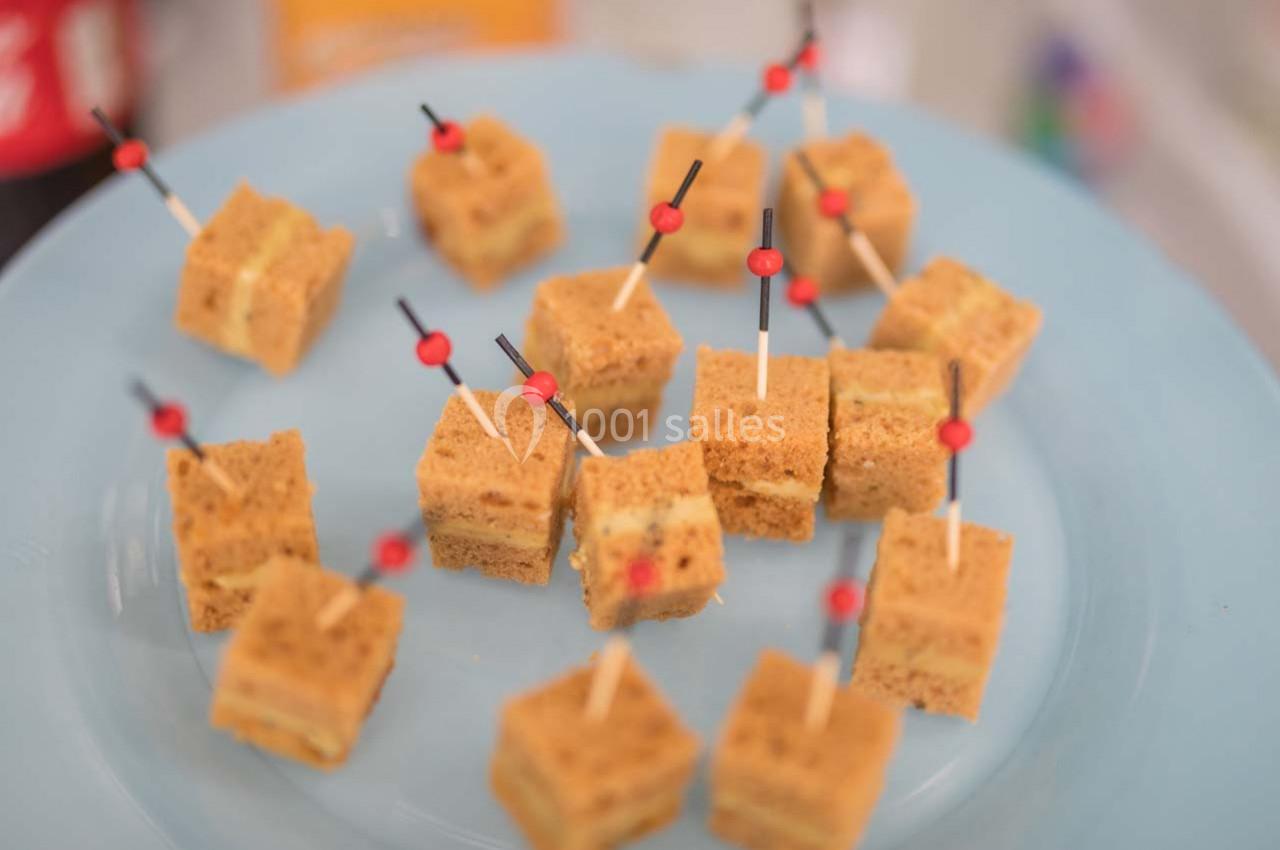 Carrés de gâteau disposés sur une assiette bleue, chacun piqué avec un cure-dent décoré d'une perle rouge.