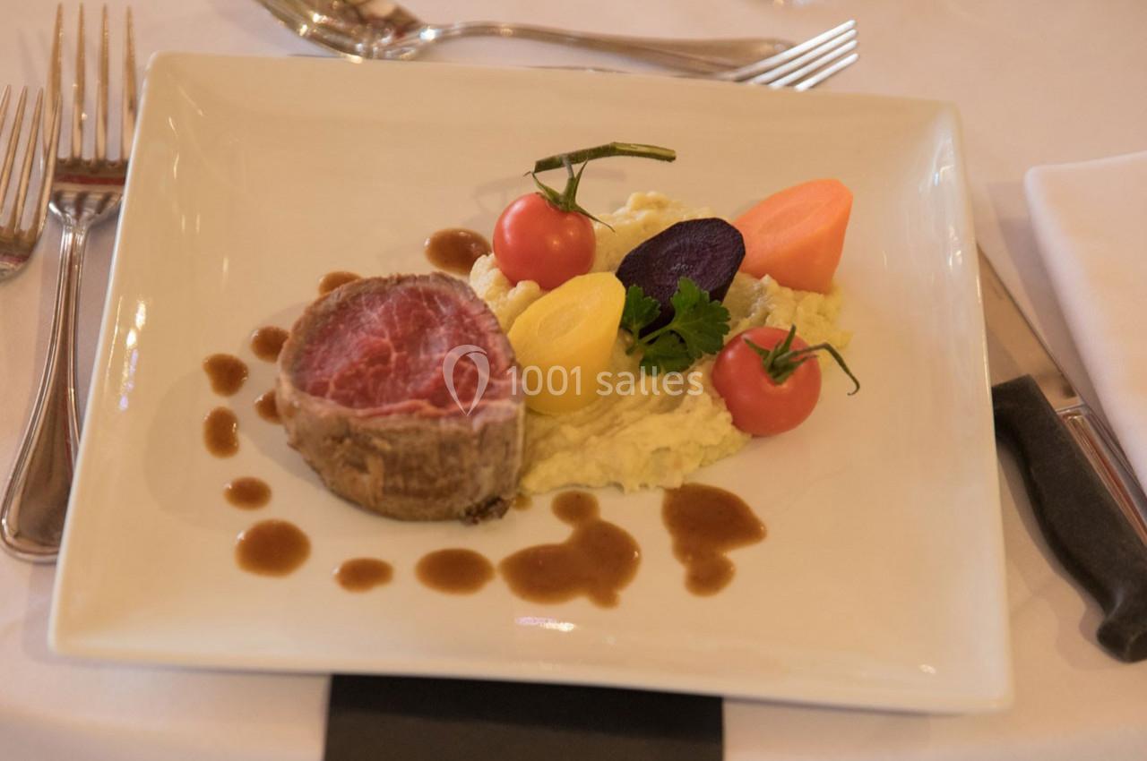 Assiette gastronomique avec filet de viande, purée, légumes colorés et sauce, servie sur une table dressée.