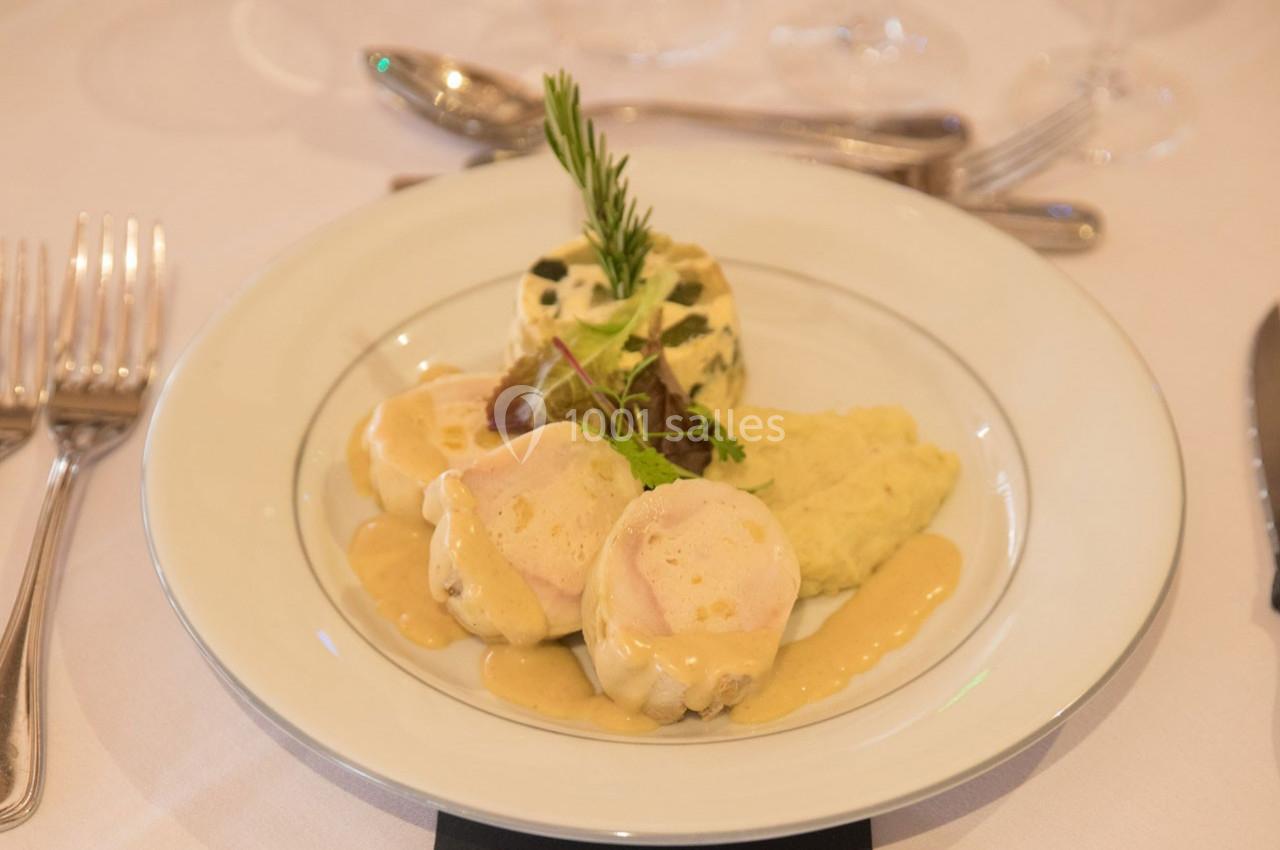 Assiette de médaillons de volaille nappés de sauce, accompagnés de purée, légumes et garniture d'herbes fraîches.