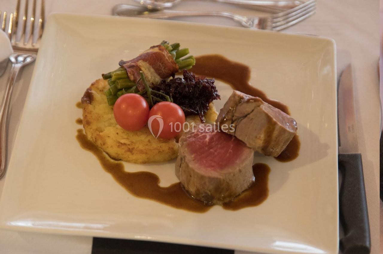 Assiette de filet de viande avec sauce, galette de pommes de terre, haricots verts enroulés de lard et tomates cerises.