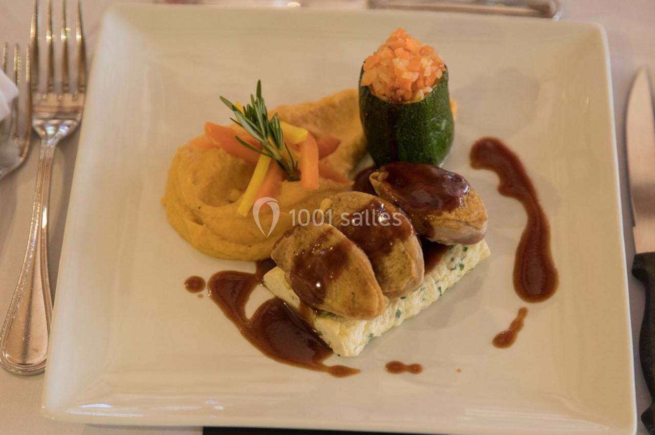 Assiette gastronomique avec viande nappée de sauce, purée, légumes décoratifs et courgette farcie sur une table dressée.