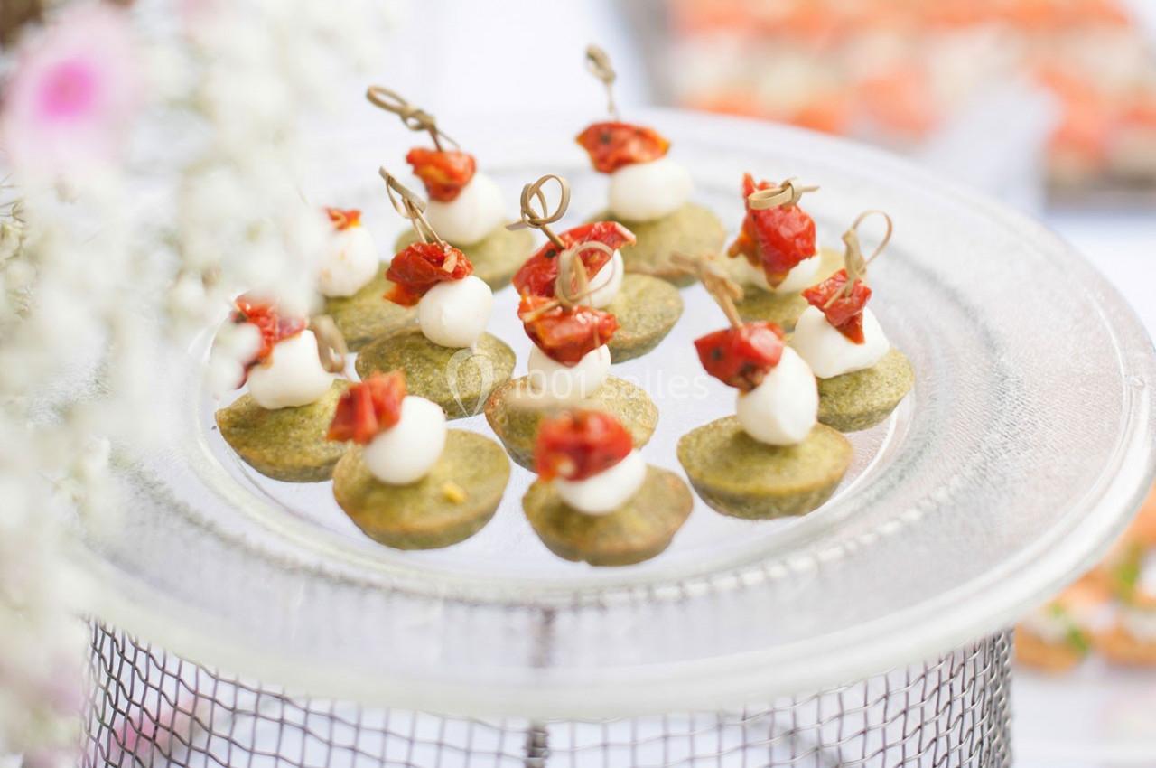 Plateau de bouchées apéritives avec tomates séchées, fromage et base verte, présenté sur un support en verre.