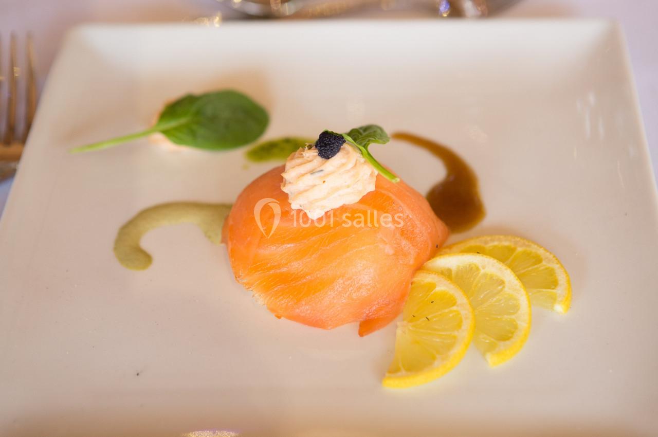 Tranche de saumon fumé garnie de crème et caviar, accompagnée de rondelles de citron et de sauce décorative.