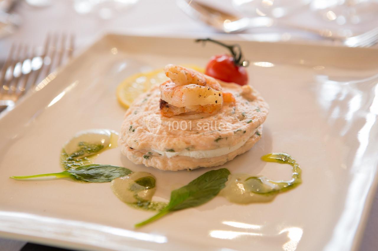 Plat raffiné composé de mousse de poisson, crevettes, tomate cerise, citron et sauce verte, présenté sur une assiette…