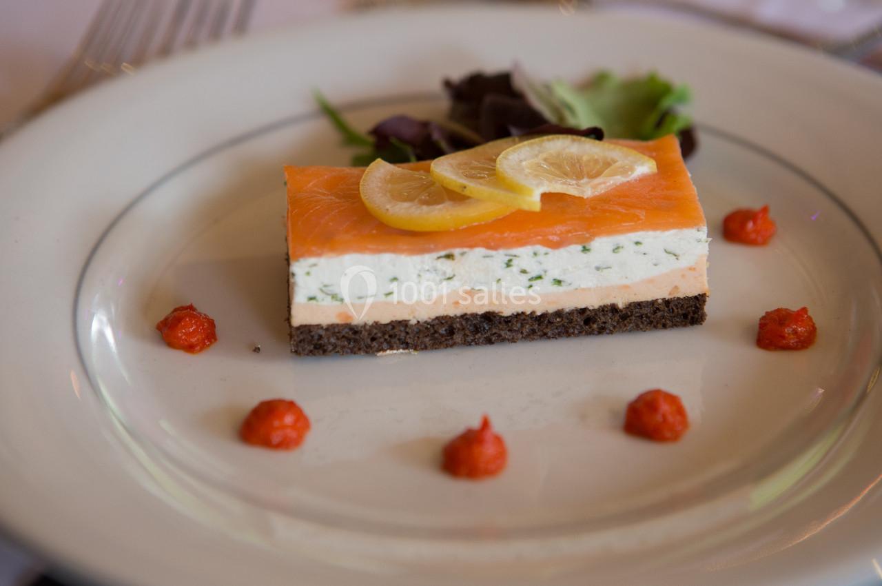 Entrée composée de saumon fumé, mousse crémeuse, pain noir, tranches de citron et décorée de points de sauce rouge.