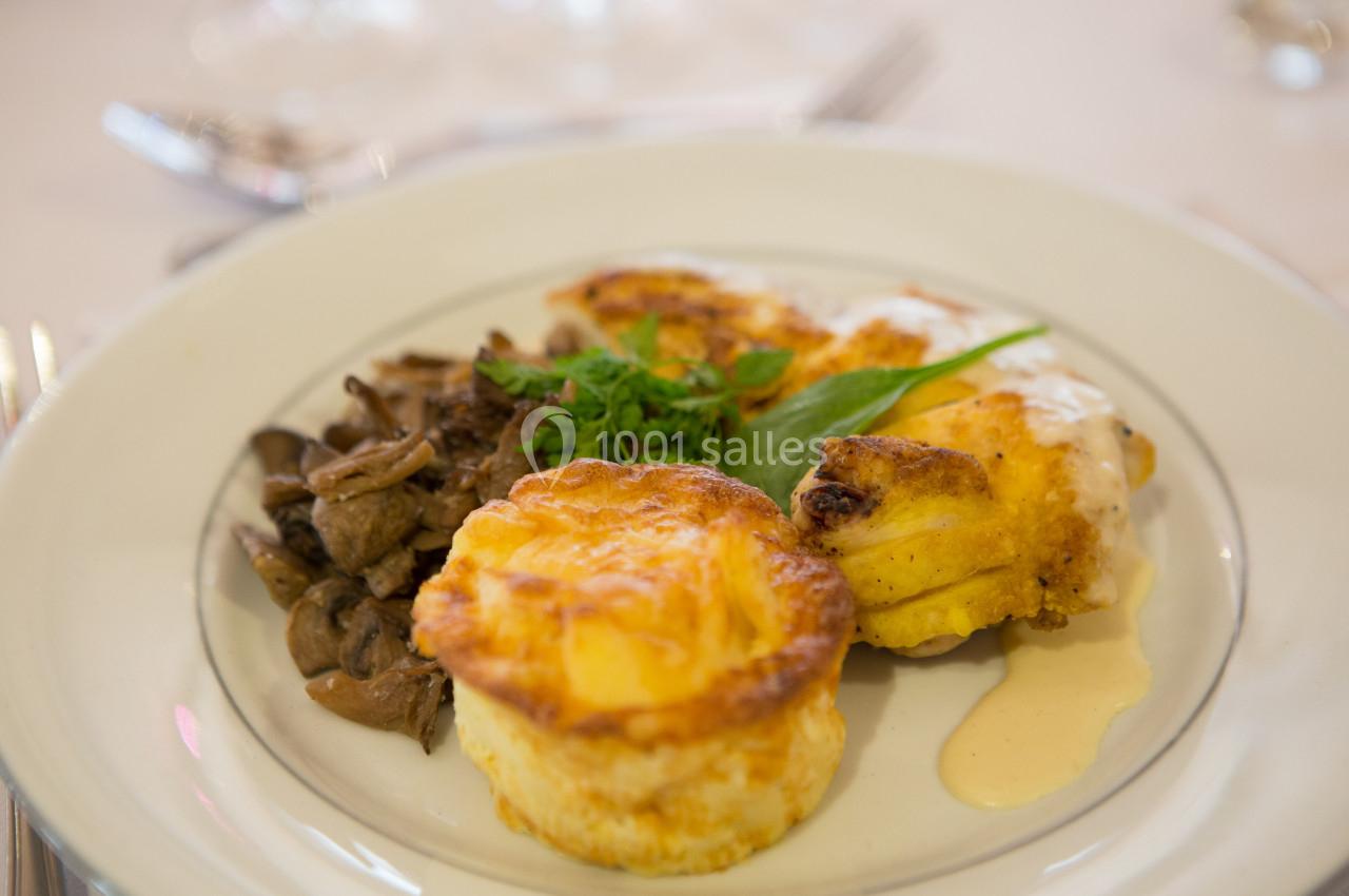 Assiette contenant un gratin individuel, du poulet en sauce et une garniture de champignons, décorée d'herbes fraîches.
