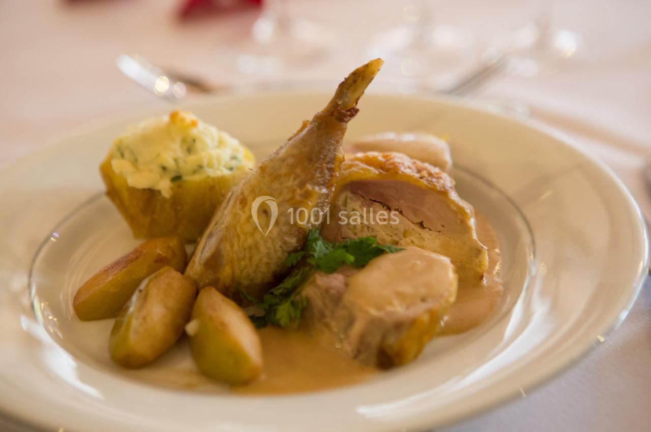 Assiette de caille rôtie servie avec pommes de terre, purée garnie et sauce, présentée sur une table dressée.