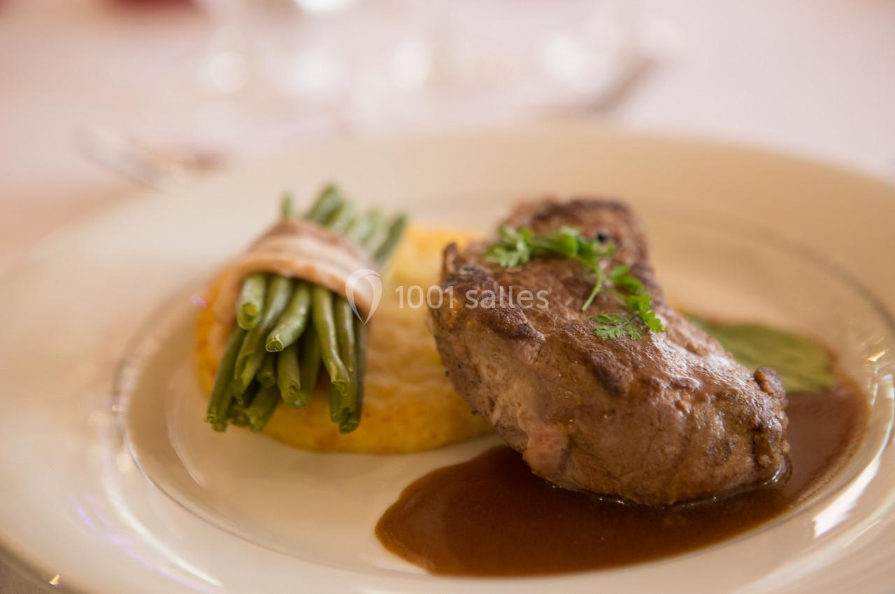 Assiette avec un filet de viande, sauce, galette de pommes de terre et haricots verts liés par une fine bande.