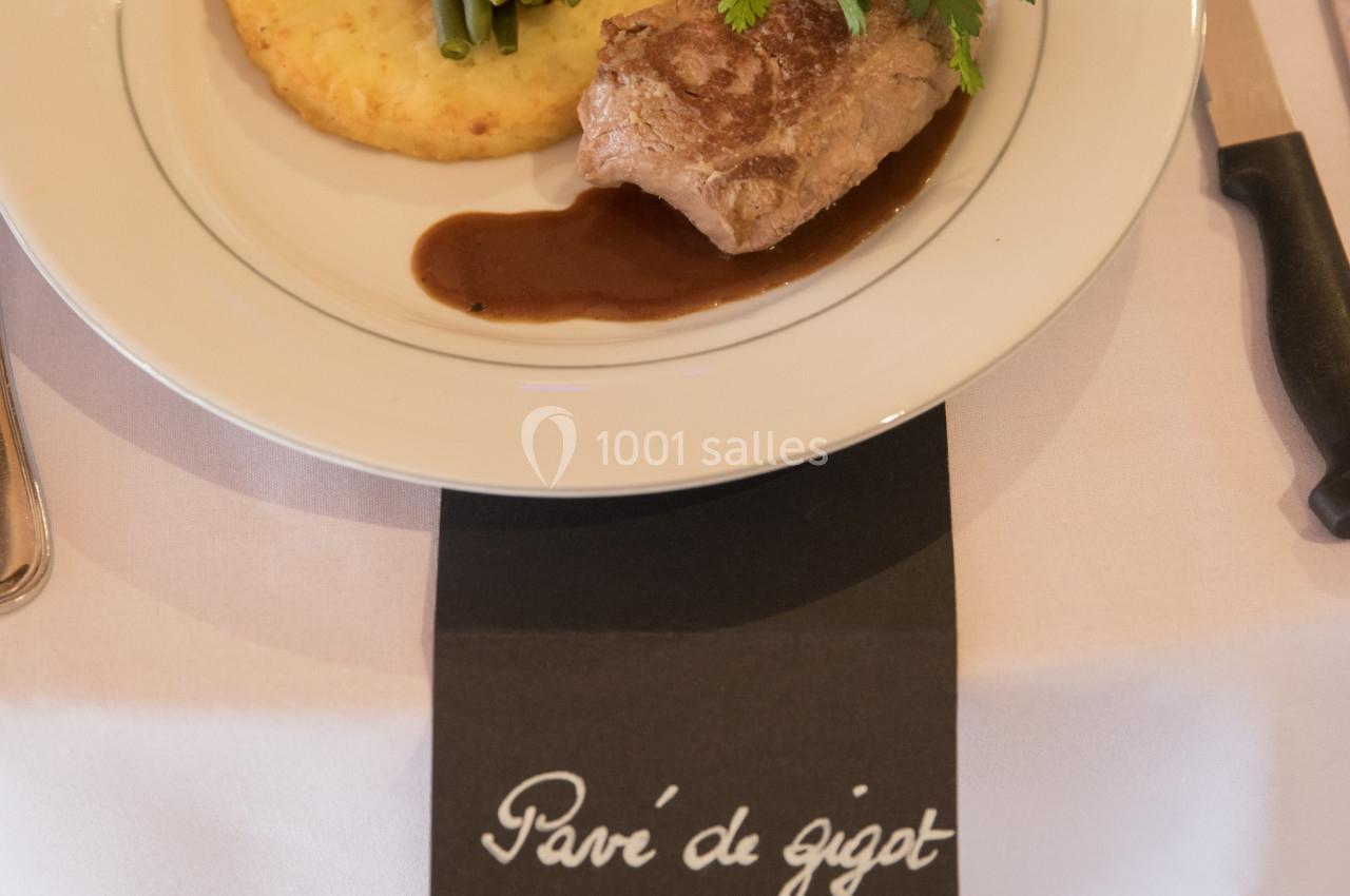 Assiette dressée avec gigot d'agneau, haricots verts enroulés de lard, galette de pommes de terre et sauce.