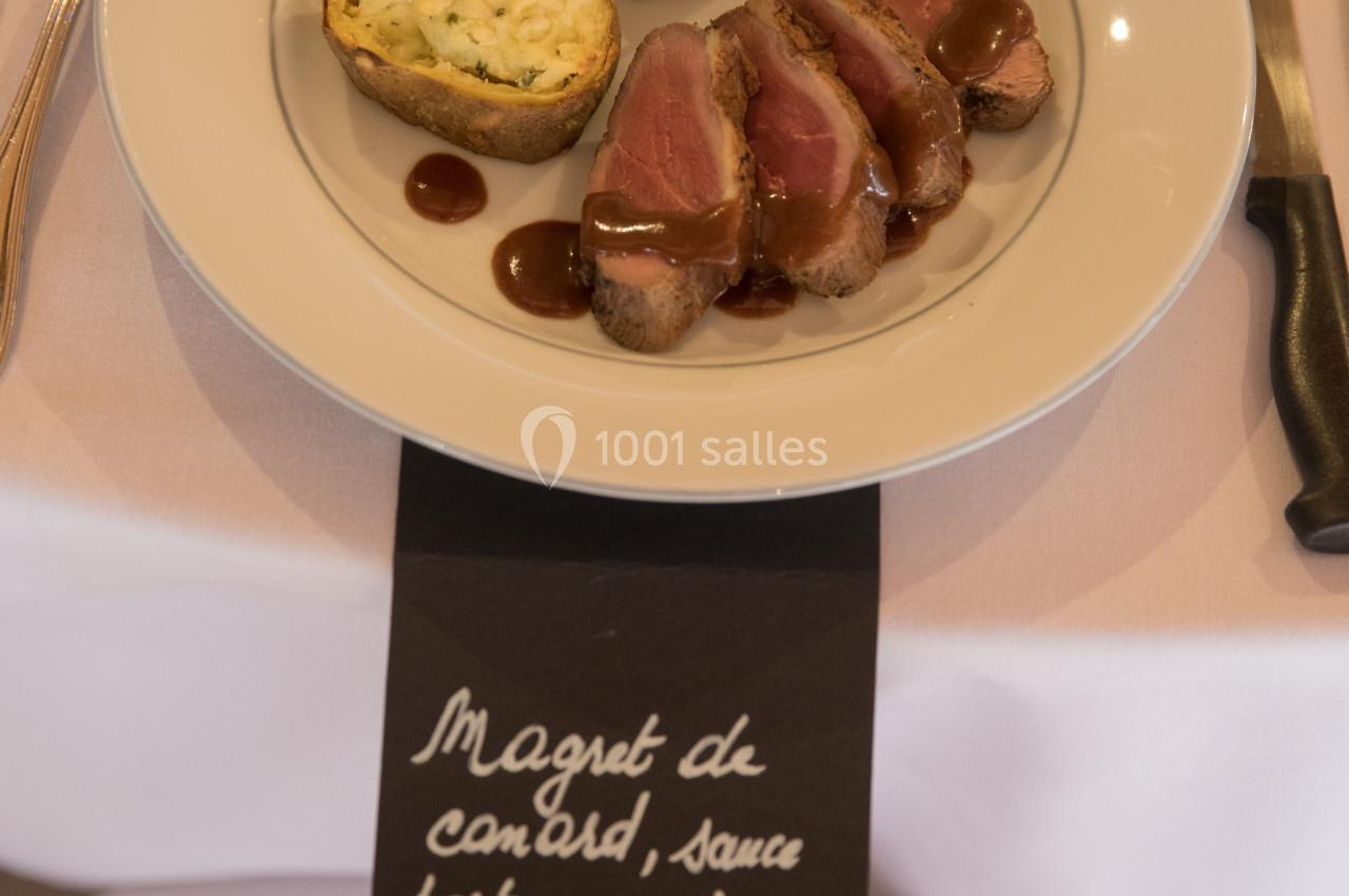 Assiette de magret de canard avec sauce, flan aux herbes et garniture, présentée sur une table dressée.