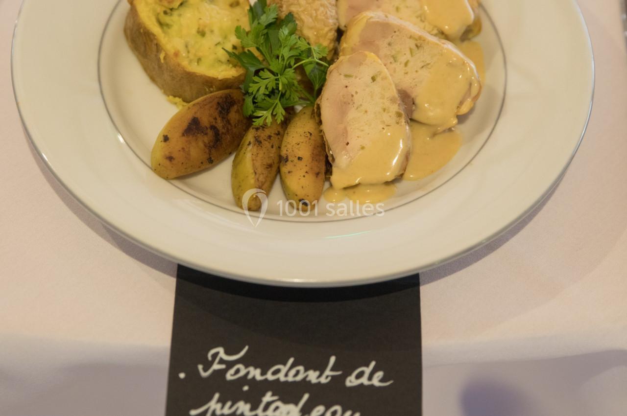 Assiette de pintade avec sauce, pommes de terre, flan de légumes et garniture de persil, servie sur une table dressée.