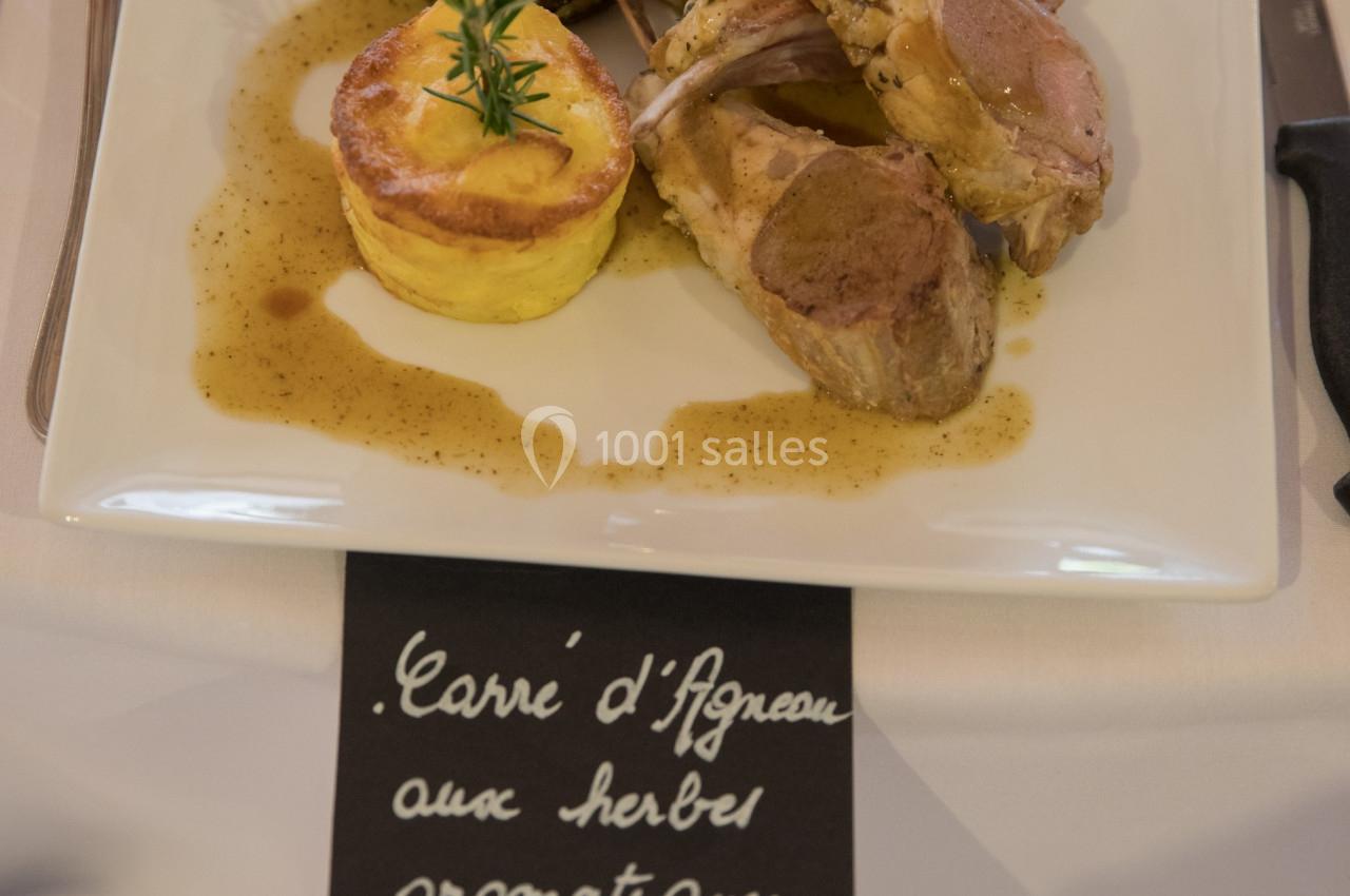 Assiette de carré d'agneau avec gratin, légumes grillés et sauce, servie sur une table dressée.