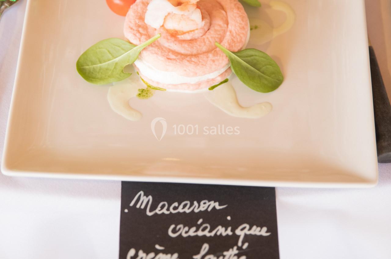 Assiette contenant un macaron rose garni de crème, accompagné de tomates cerises, citron et feuilles de salade.