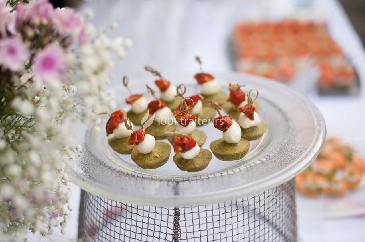 Plateau de bouchées apéritives avec tomates cerises, fromage et base verte, posé sur une table décorée de fleurs.