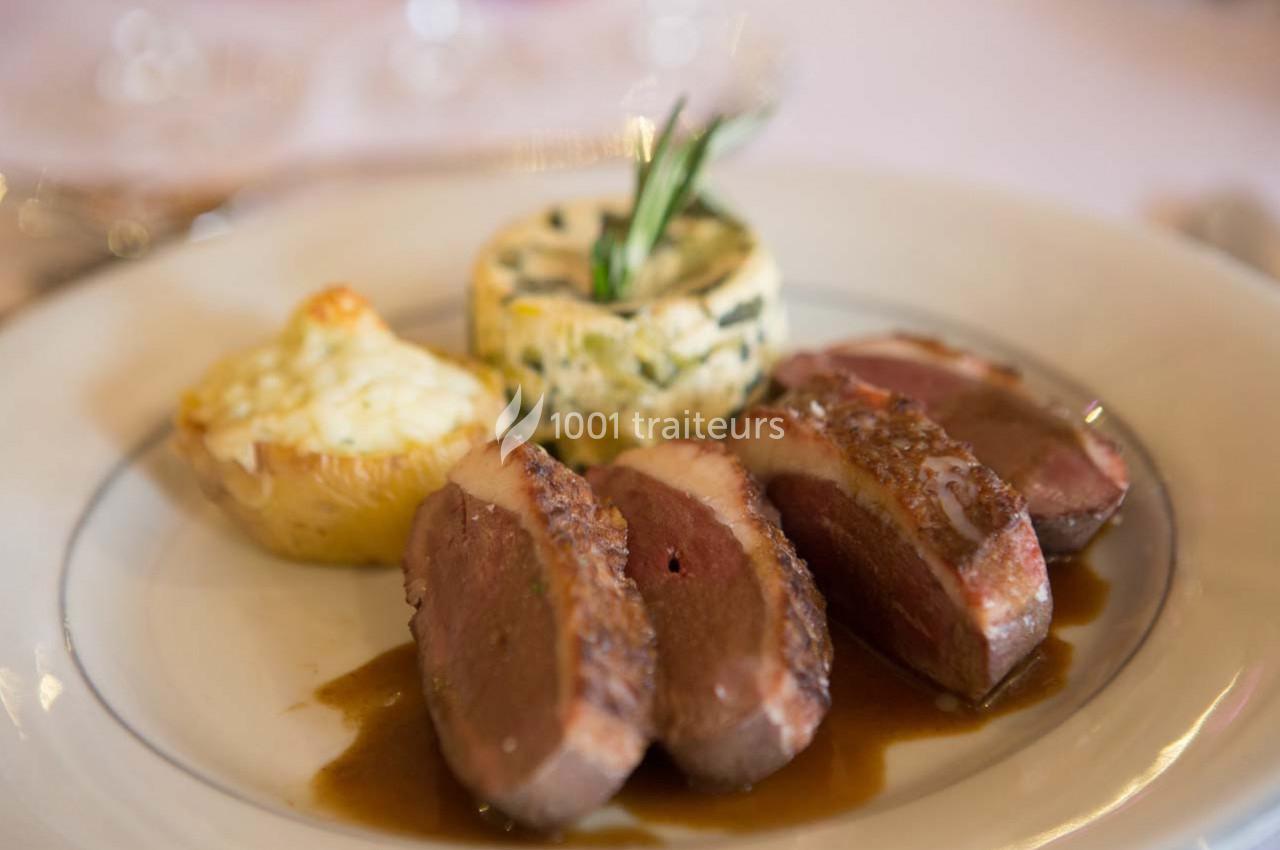 Assiette contenant des tranches de magret de canard, une pomme de terre gratinée et un flan aux légumes.