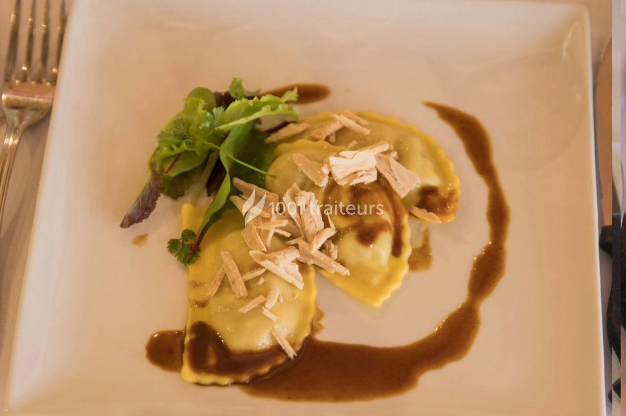 Assiette de raviolis garnis, nappés de sauce brune, décorés de copeaux et accompagnés de jeunes pousses.