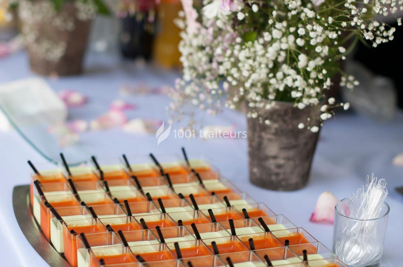 Plateau de verrines colorées alignées sur une table décorée de fleurs et de pétales.