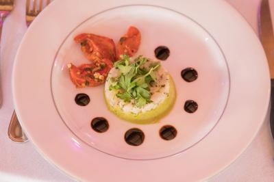 Assiette contenant une mousse verte garnie de persil, accompagnée de tomates rôties et de points de sauce balsamique.
