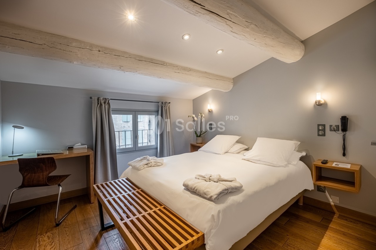 Chambre lumineuse avec lit double, bureau en bois, poutres apparentes et fenêtre donnant sur l'extérieur.