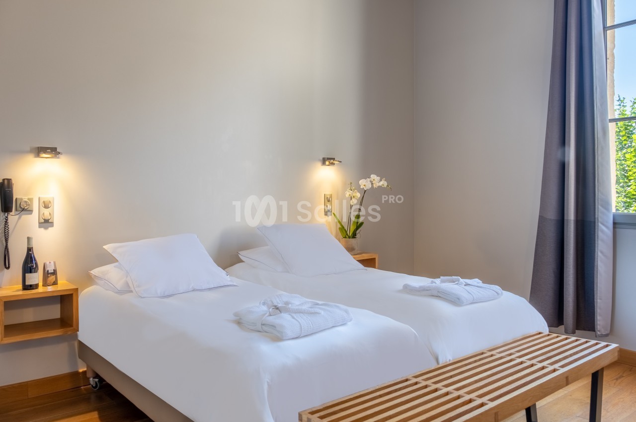 Chambre lumineuse avec deux lits simples, tables de chevet en bois, orchidée blanche et fenêtre donnant sur l'extérieur.