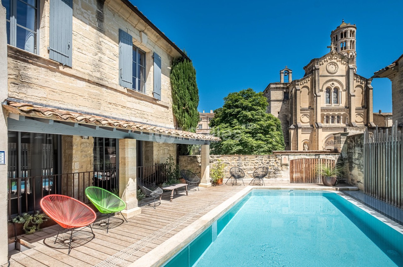 Cour avec piscine, chaises colorées et vue sur une église en pierre sous un ciel bleu.