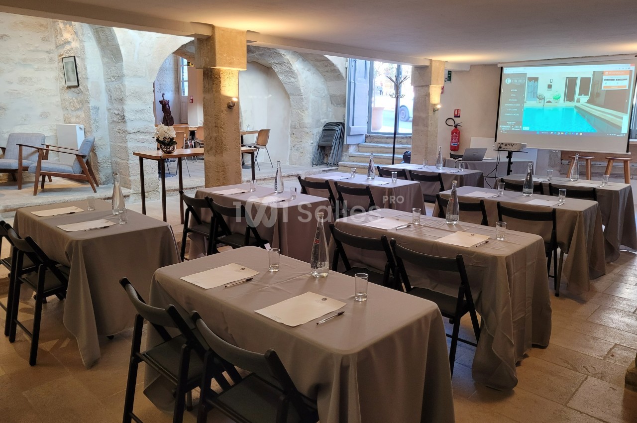 Salle de réunion lumineuse avec tables, chaises, bouteilles d'eau et écran de projection installé à l'avant.