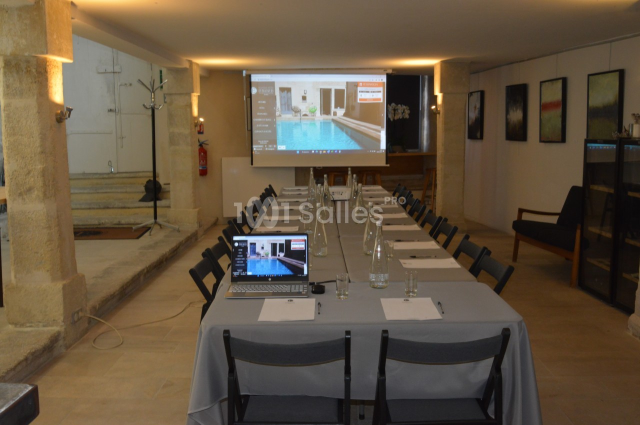 Salle de réunion équipée avec un projecteur, un écran, des tables disposées en U et un ordinateur portable.