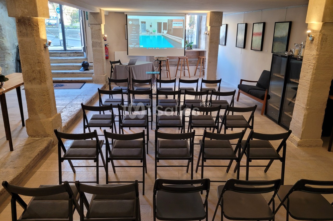 Salle de réunion avec des chaises alignées face à un écran de projection, éclairée par une lumière naturelle et artificielle.