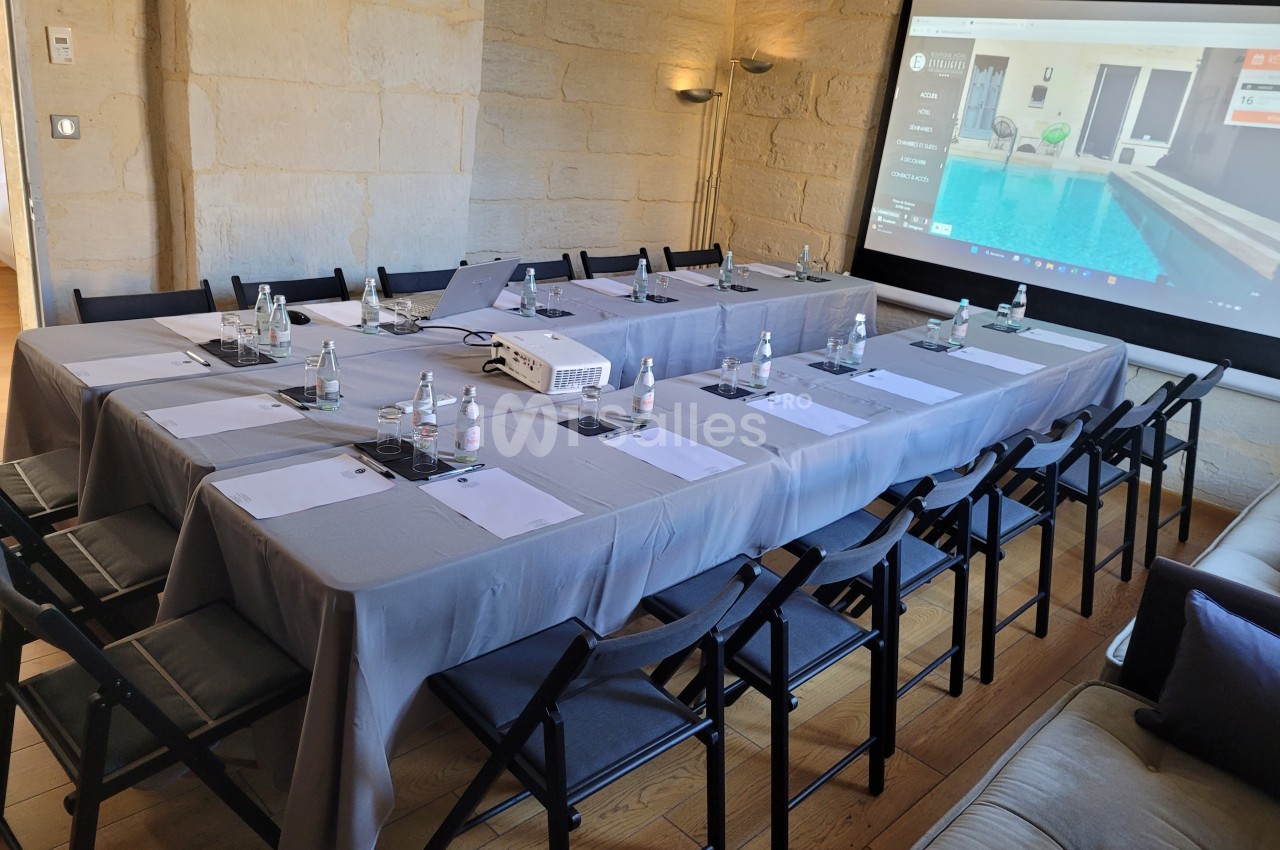 Salle de réunion avec une grande table rectangulaire, chaises noires, projecteur et écran affichant une image de piscine.