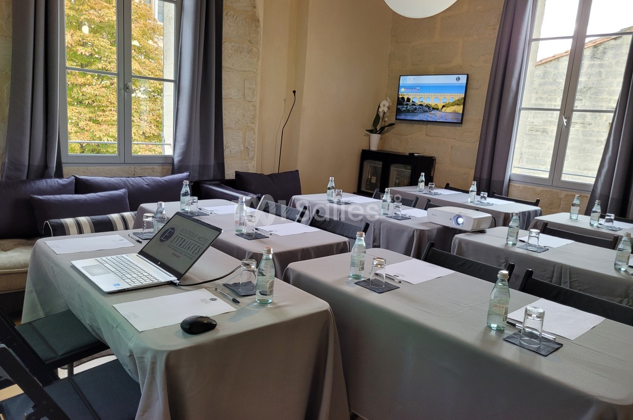 Salle de réunion lumineuse avec tables dressées, ordinateurs portables, bouteilles d'eau et écran de présentation.