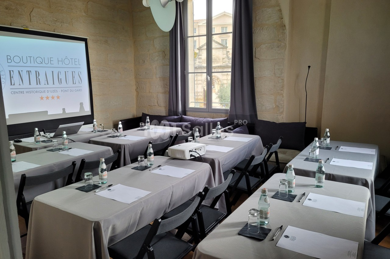 Salle de réunion lumineuse avec tables, chaises, bouteilles d'eau, blocs-notes et un écran de projection.