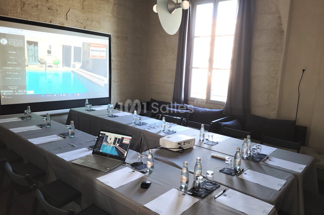 Salle de réunion équipée avec projecteur, ordinateur portable et documents disposés sur des tables en U.