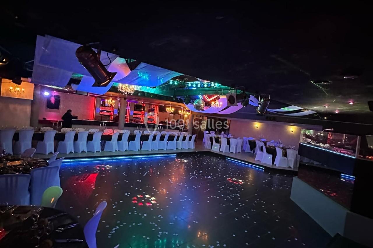 Salle de réception avec piste de danse illuminée, tables dressées et éclairage coloré dans une ambiance festive.