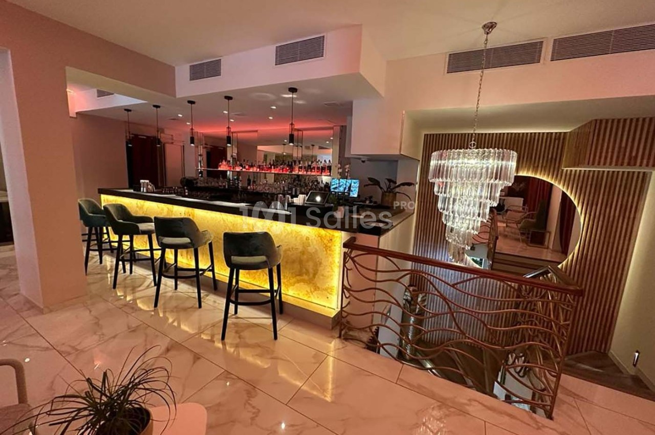 Bar moderne avec comptoir éclairé, tabourets hauts, lustre en cristal et ambiance chaleureuse dans un espace élégant.