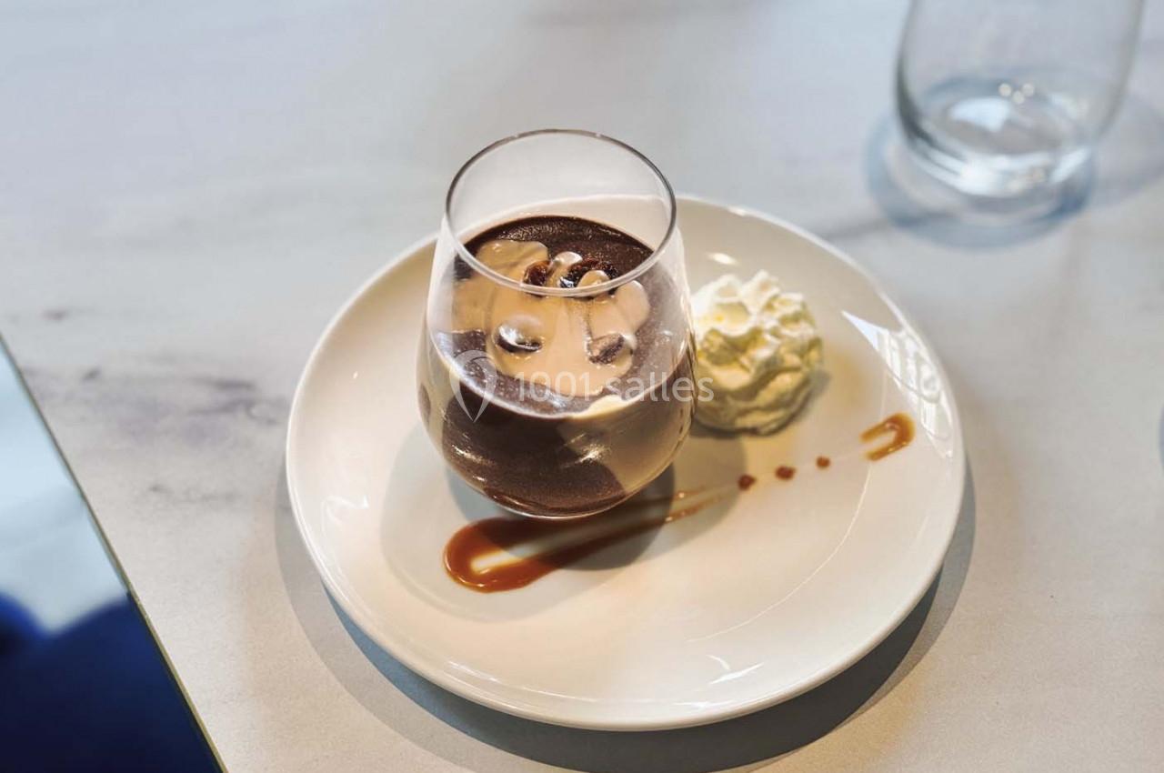 Verre de dessert au chocolat avec chantilly et filet de caramel sur une assiette blanche, posé sur une table claire.