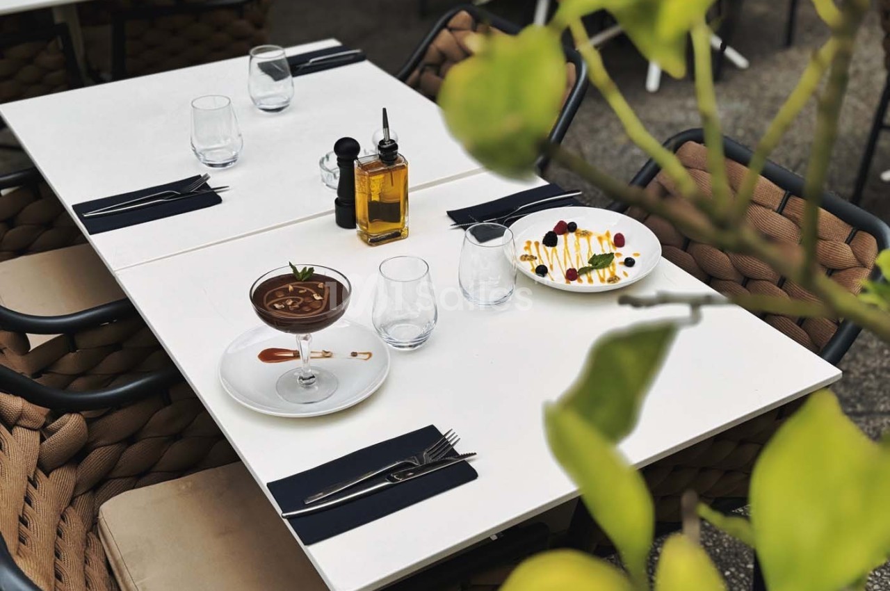 Table dressée en extérieur avec un dessert au chocolat, une assiette colorée, de l'huile d'olive et des verres vides.