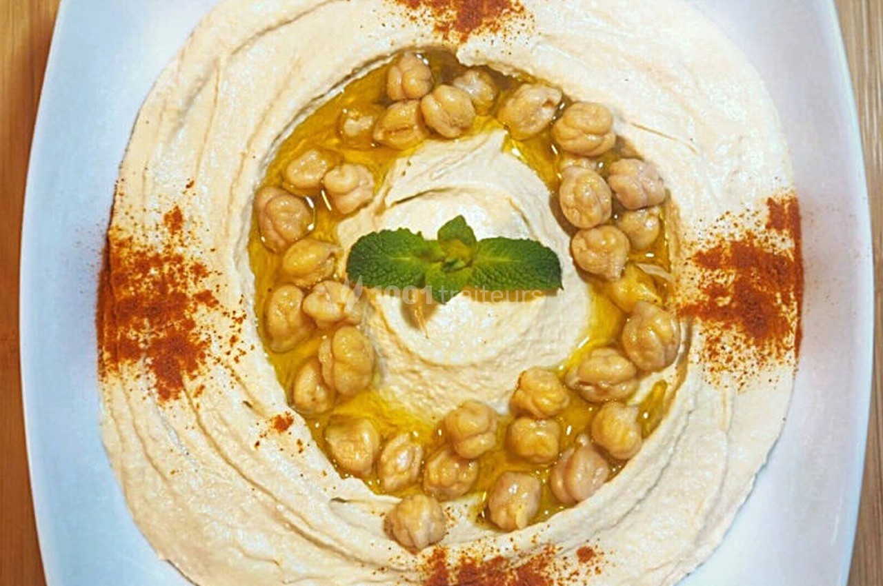 Assiette de houmous garni de pois chiches, huile d'olive, paprika et feuilles de menthe, présentée sur une table en bois.