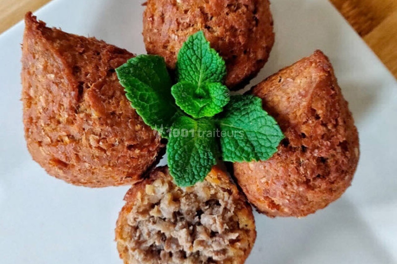 Quatre kibbeh dorés disposés en fleur sur une assiette blanche, garnis de feuilles de menthe fraîche.